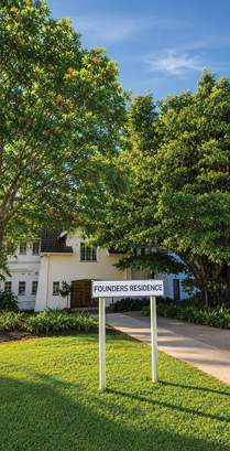 A white building labeled “Founders Residence" is partially visible behind green trees with a clear blue sky above. Description generated by AI